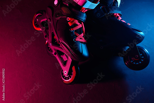 Close up view of roller skates inline skate or rollerblading on dark grunge background in neon blue magenta pink light