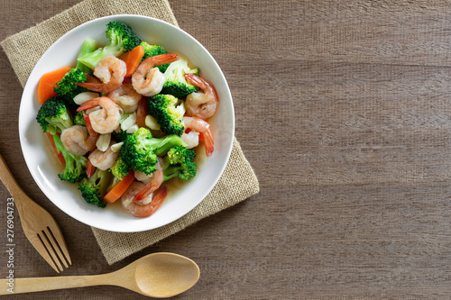 top view of stir fried broccoli with shrimps in a ceramic dish on wooden table. homemade style food concept.