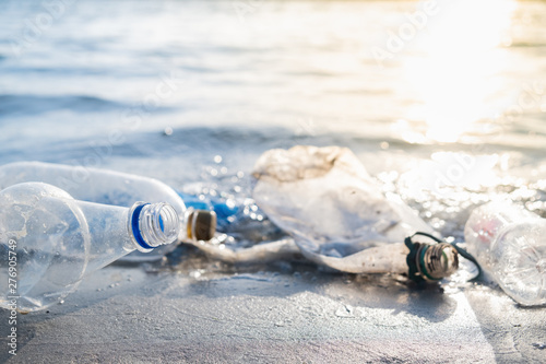 Empty plastic bottles on the beach, seashore and water pollution concept. Trash (empty beverage packages) thrown away at the seaside, close-up view in direct sunlight