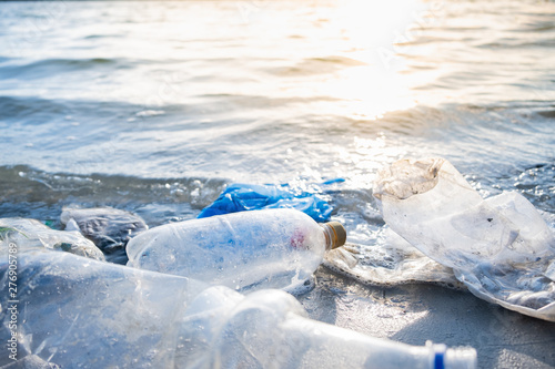 Empty plastic bottles on the beach, seashore and water pollution concept. Trash (empty beverage packages) thrown away at the seaside, close-up view in direct sunlight