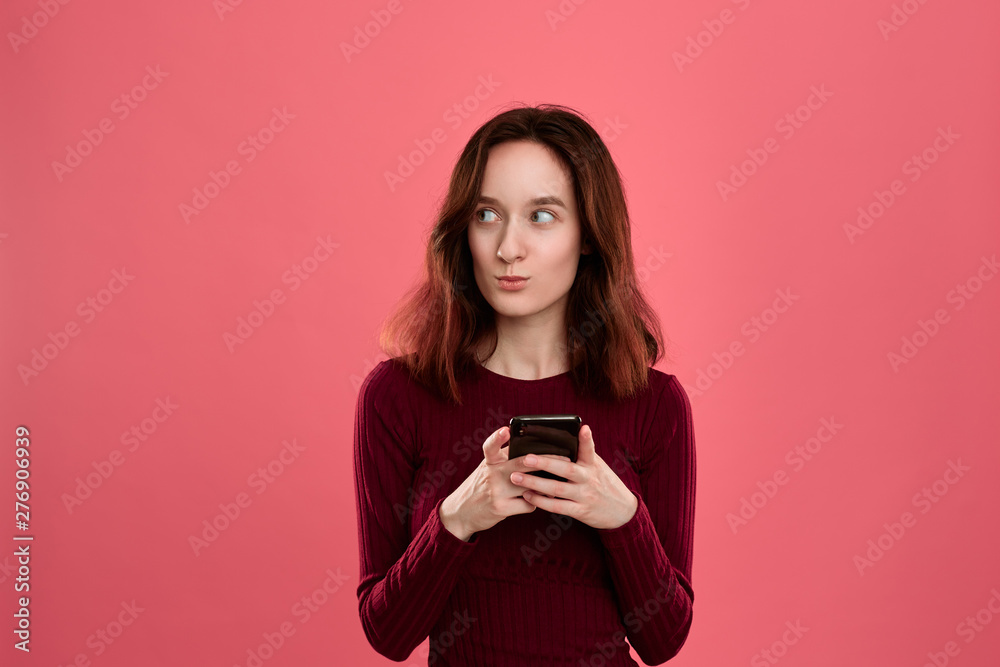 Portrait of a pretty brunette girl standing on a dark pink background and texting on the phone. Portrait of a pretty brunette girl standing on a dark pink background and texting on the phone.