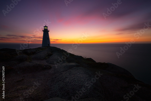 Silhouette of a white lighthouse sitting at the edge of a rocky cliff as purple and orange colors light up the early morning sky. Cape Spear National Historic Site, St Johns Newfoundland. 