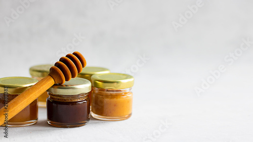 Five Small glass jar with metal cap with different kinds and colours of honey put in line and wooden spoon isolate and on grey cement background, copy space. Healthy product, natural Horizontal banner