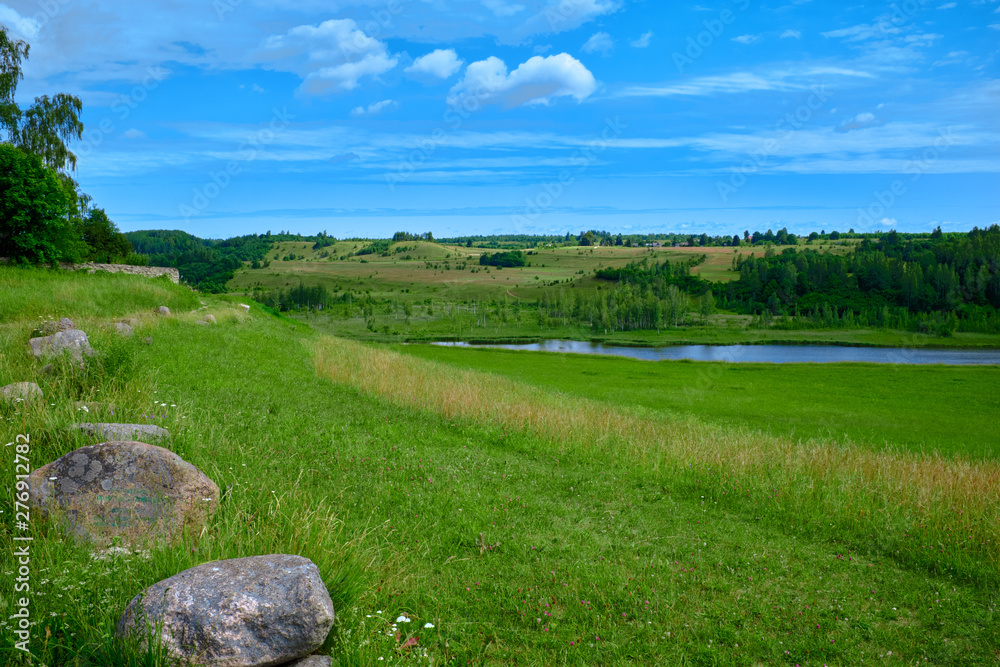 Sunny summer landscape with river. Green hills and meadows. Fields of lush green grass.