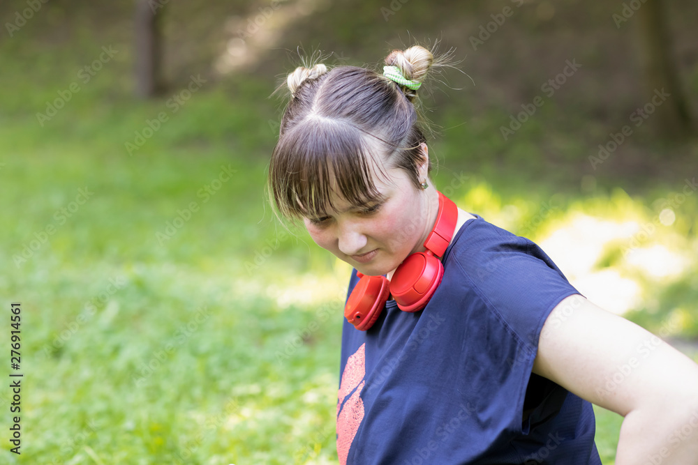 Portrait of a teenage girl sitting on the grass in a city park in a blue t-shirt and jeans with red headphones. Portrait of a teenage girl sitting on the grass in a city park in a blue t-shirt and jeans with red headphones.