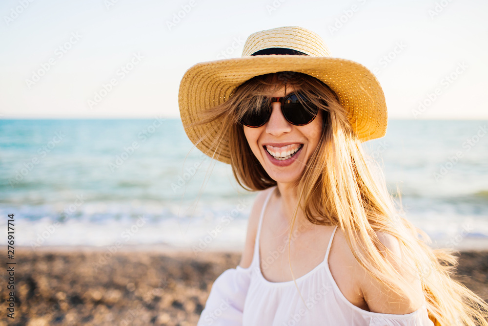 Young happy attractive girl in straw hat relaxing at the beach. Sunny weather and blue waves on the background.
