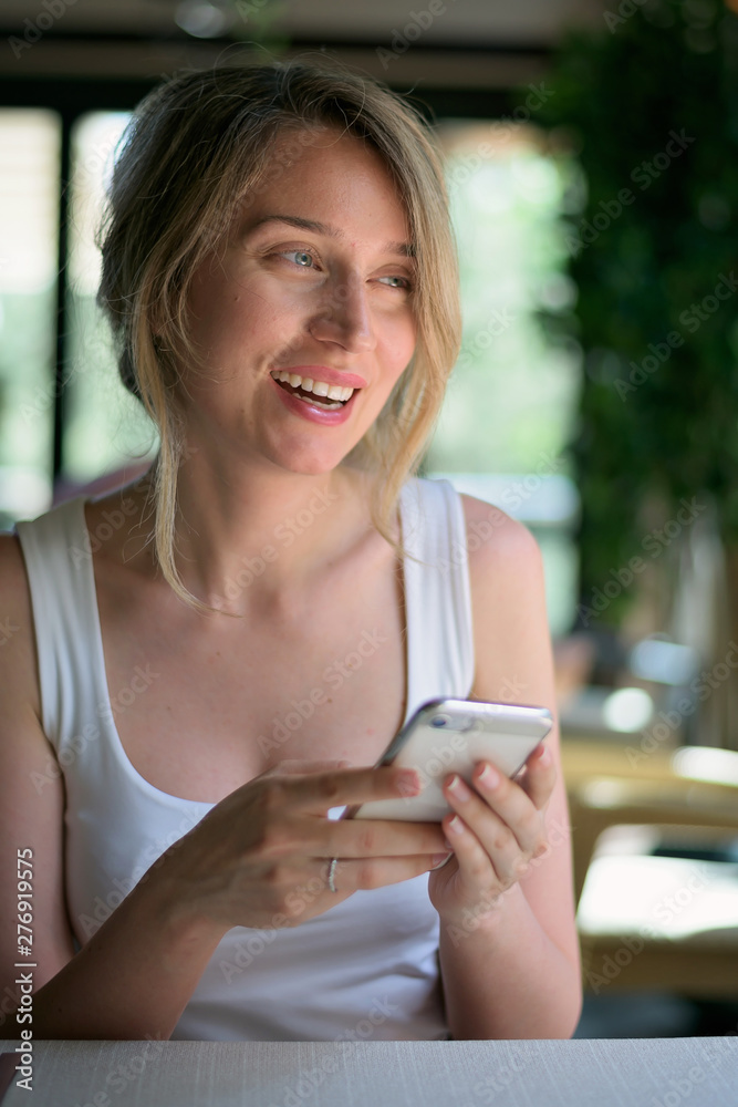 Happy young blonde woman talking on the phone in a restaurant at business lunch Happy young blonde woman talking on the phone in a restaurant at business lunch