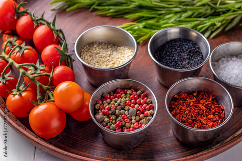 Spices: a mixture of peppers, paprika flakes, sea salt, black and white sesame, rosemary and cherry tomatoes on a plate close-up