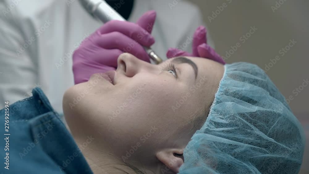 beauty salon visitor lies and woman in white coat applies permanent eyebrow make-up close view beauty salon visitor lies and woman in white coat applies permanent eyebrow make-up close view