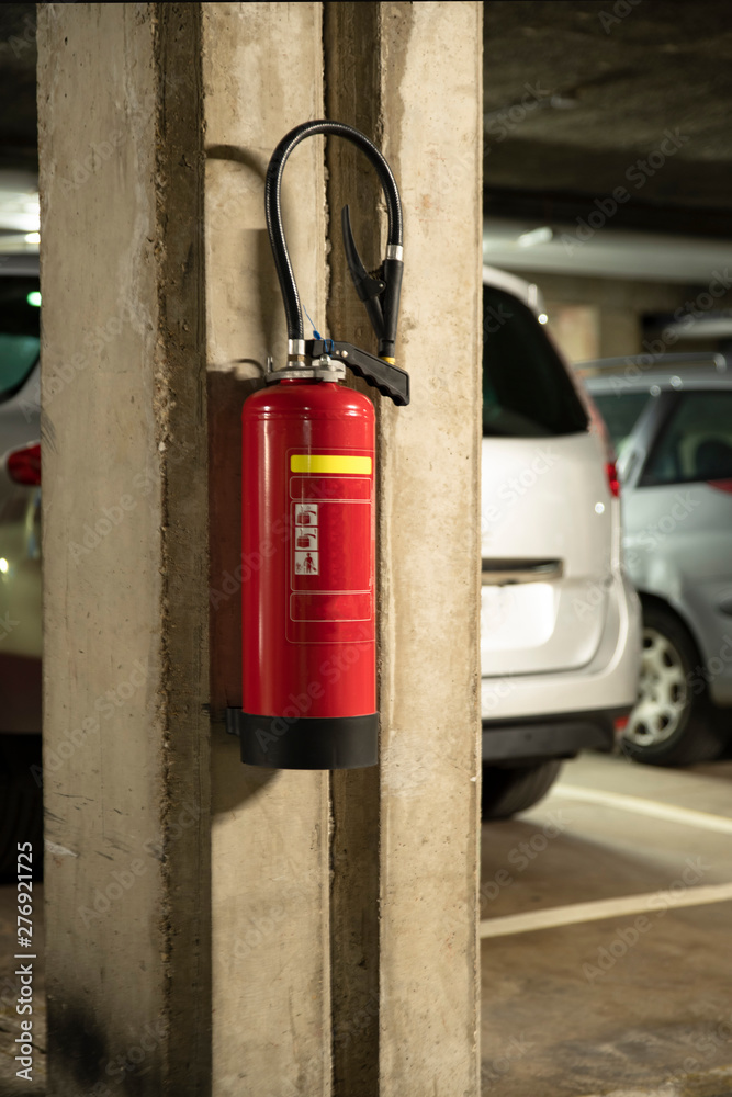 Fire extinguisher hung on a wall in a car park with cars