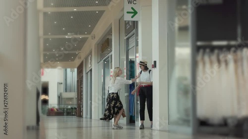 View of a hurrying blonde girl rushing to the toilet asking in a long queue to let her to the restroom. Impatient young woman squirting of pain running inside the toilet pushing another girl.