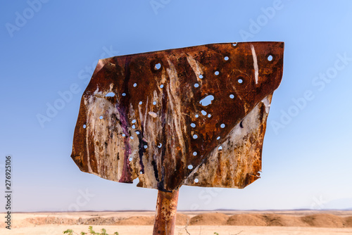 Old metal sign covered in rust and filled with holes after being shot at with a shotgun.