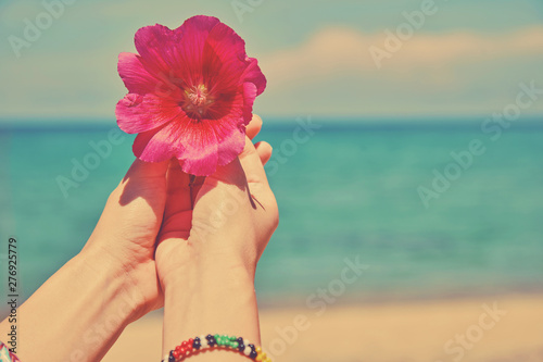Woman holding wild flower on the tropical sandy beach.