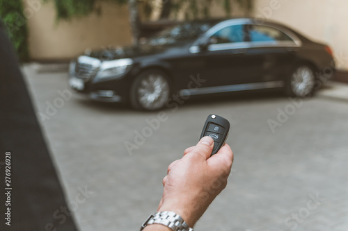 The man opens the car with a keychain, in the background is a black car.