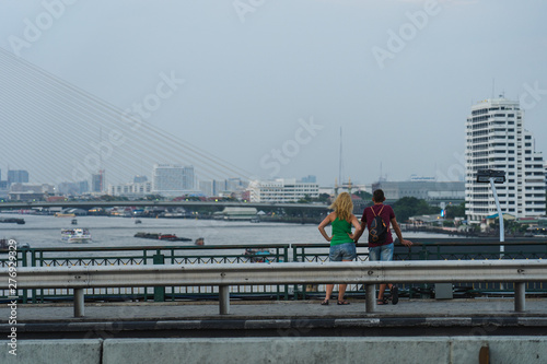 a couple of tourist is enjoying the view of Bangkok city  and biggest river in the Bangkok with huge bridge over the river
