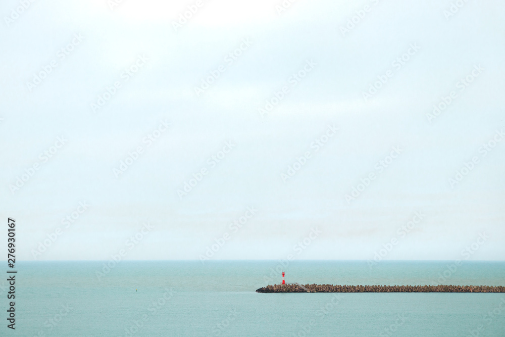 Lighthouse in sea on embankment. Red lighthouse on horizon background. Light tower in middle of sea. Beacon points the way. Light station on skyline