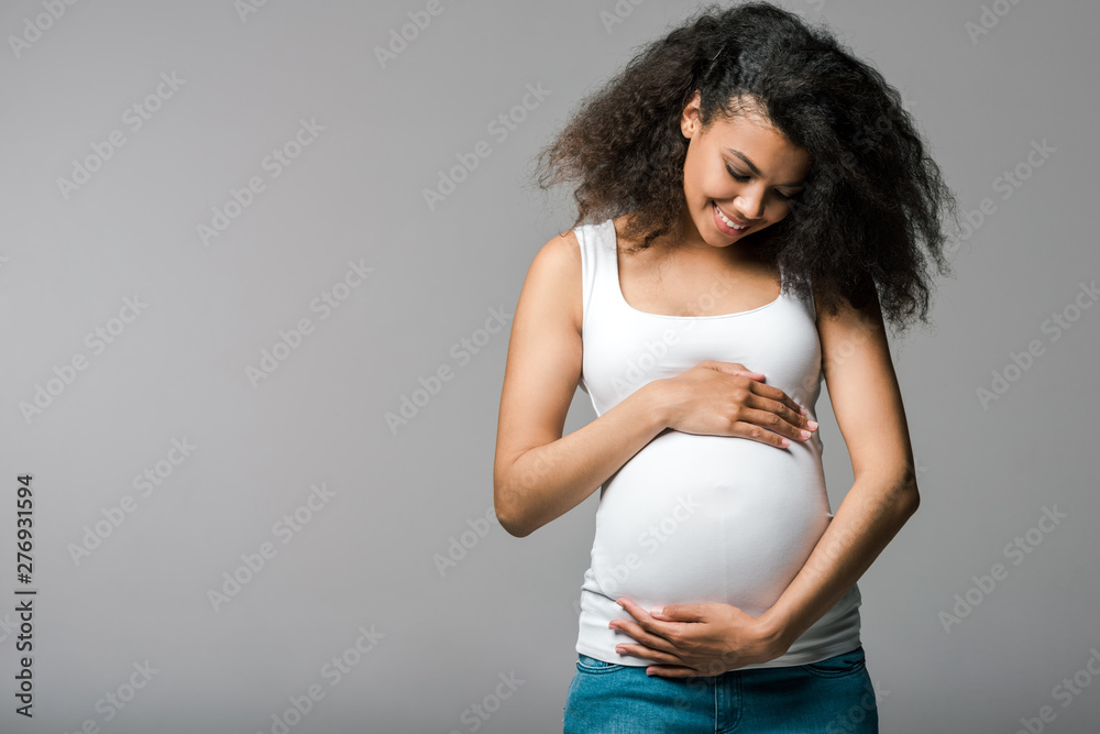 cheerful pregnant african american girl touching belly on grey - obrazy, fototapety, plakaty 