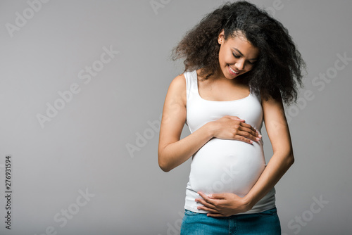 Canvas Print cheerful pregnant african american girl touching belly on grey