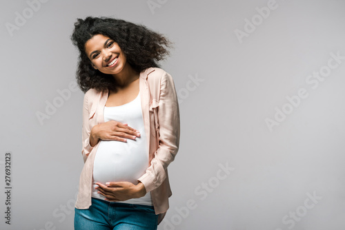 Photo happy young pregnant african american woman touching belly on grey