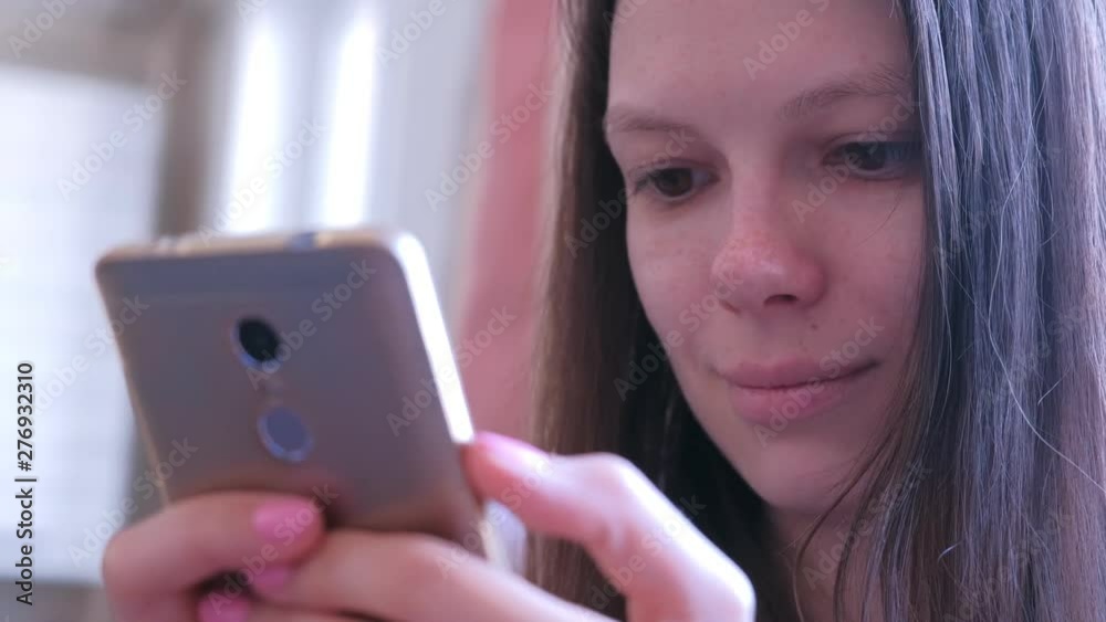 Young woman is reading a book on smartphone. She is looking at screen moving her eyes. Portrait of brunette girl online browsing and surfing web internet pages. Young woman is reading a book on smartphone. She is looking at screen moving her eyes. Portrait of brunette girl online browsing and surfing web internet pages.