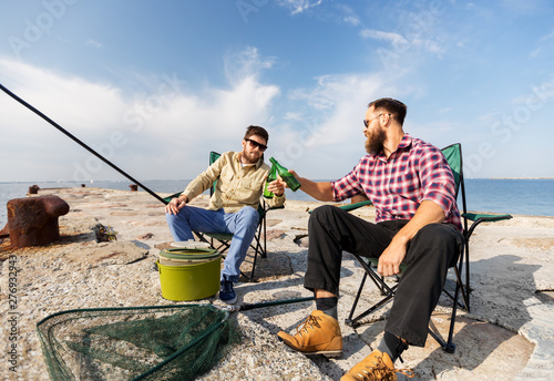leisure and people concept - male friends fishing and drinking beer on sea pier