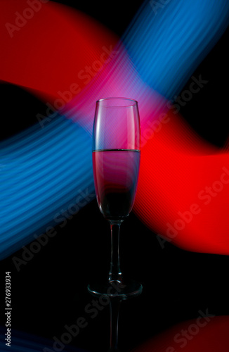 A single wine glass isolated on a black background with red white pink and orange neon light painting streaks of light behind them. Light wave, game of colors, drawing light.