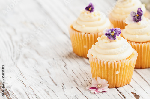 Beautiful vanilla cupcakes with buttercream icing decorated with sugar coated violet flowers. Selective focus with blurred background.