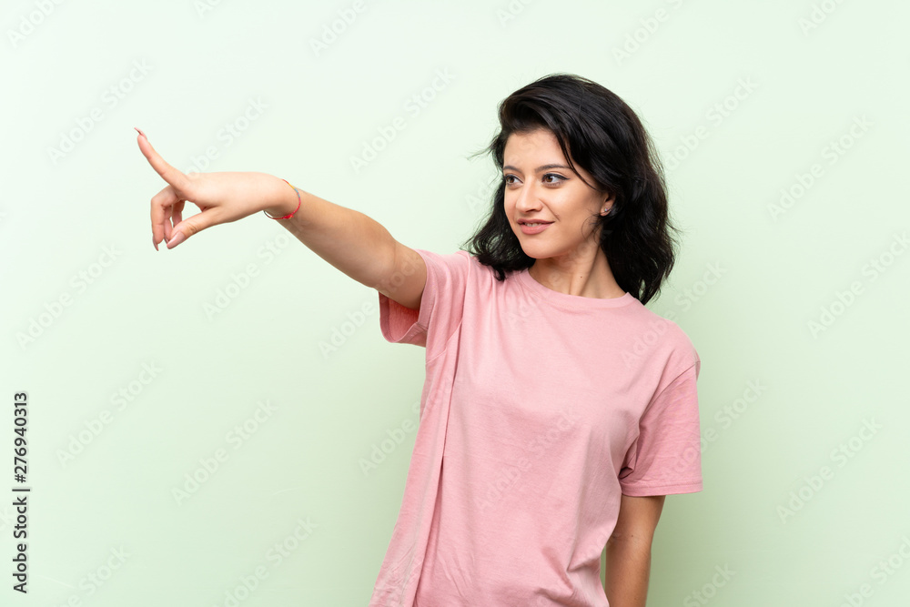 Young woman over isolated green background pointing away