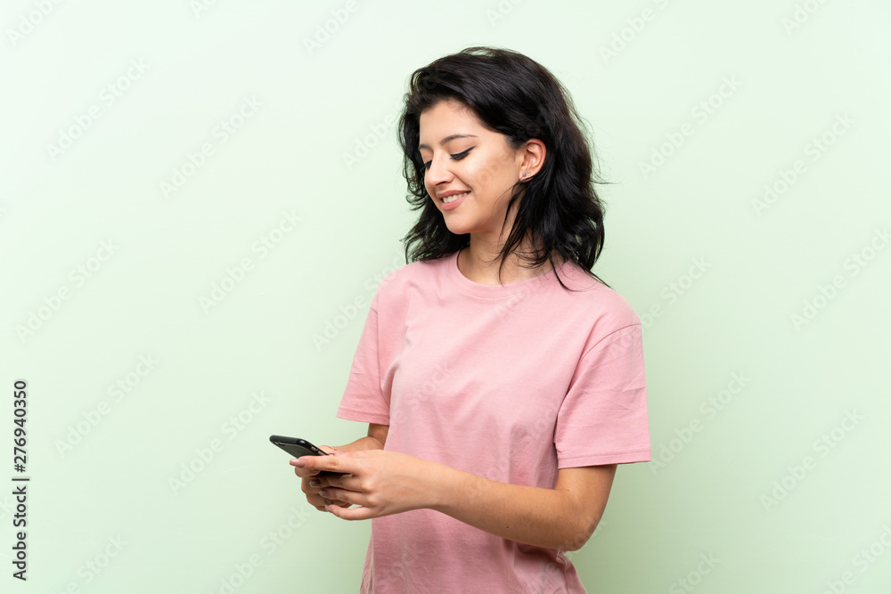 Young woman over isolated green background sending a message with the mobile Young woman over isolated green background sending a message with the mobile