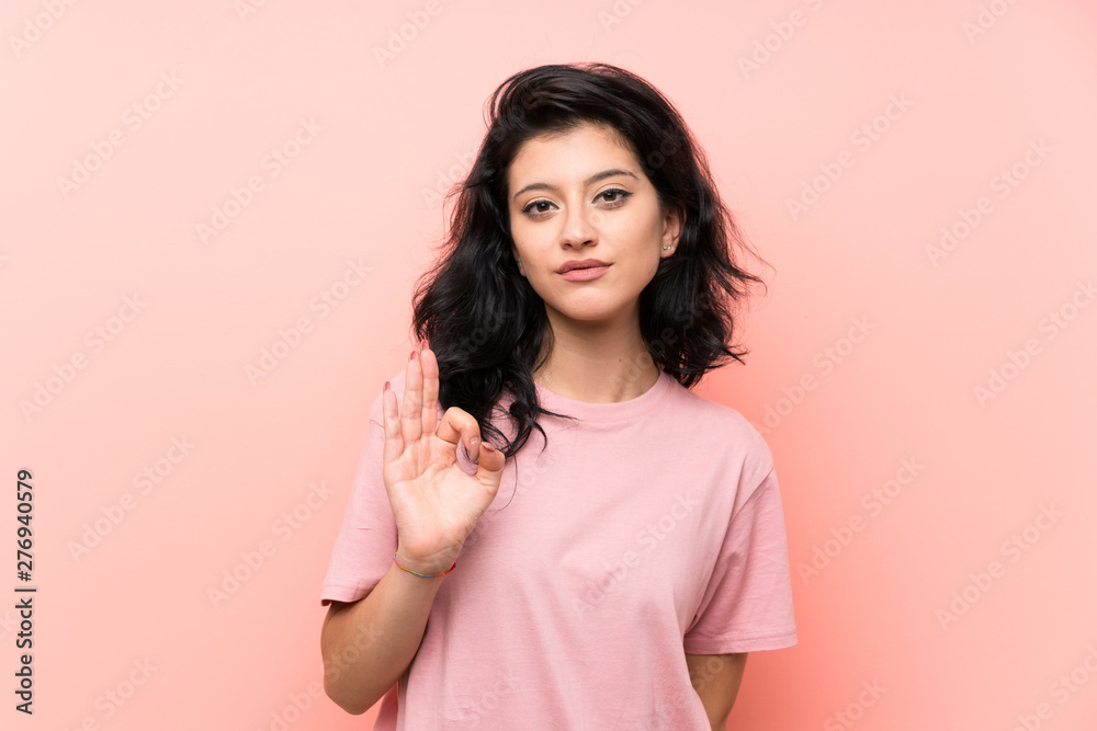 Young woman over isolated pink background showing an ok sign with fingers Young woman over isolated pink background showing an ok sign with fingers