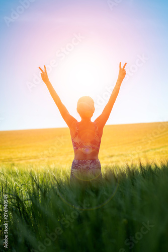 Back view of a woman at sunrise with her arms raised in joy and freedom