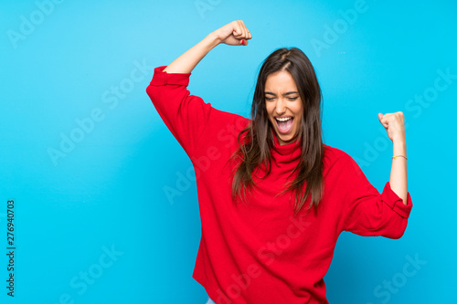 Young woman with red sweater over isolated blue background celebrating a victory