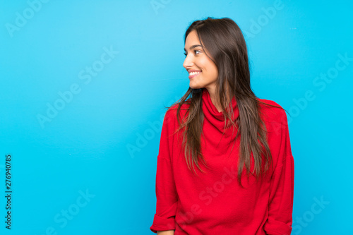 Young woman with red sweater over isolated blue background looking to the side