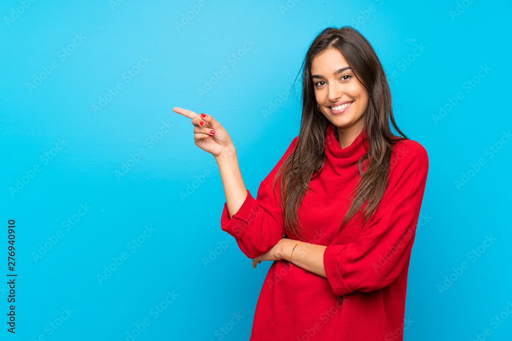 Young woman with red sweater over isolated blue background pointing finger to the side Young woman with red sweater over isolated blue background pointing finger to the side