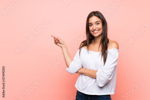 Young woman over isolated pink background pointing finger to the side