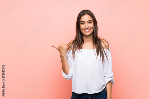 Young woman over isolated pink background pointing to the side to present a product