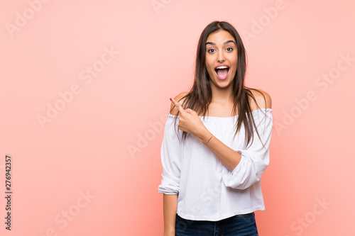 Young woman over isolated pink background surprised and pointing side