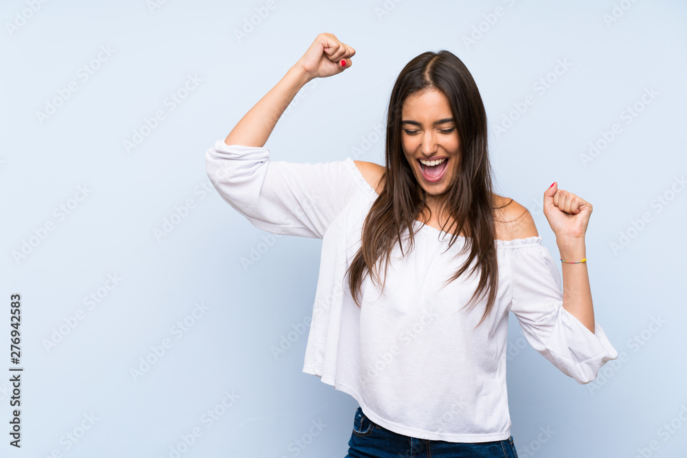 Young woman over isolated blue background celebrating a victory