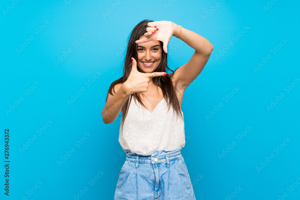 Young woman over isolated blue background focusing face. Framing symbol Young woman over isolated blue background focusing face. Framing symbol