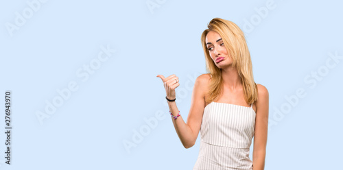 Young blonde woman unhappy and pointing to the side over isolated blue background
