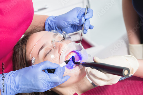 Close-up of a dentist and nurse making a dried new filling with ultraviolet young female patient in the dental office