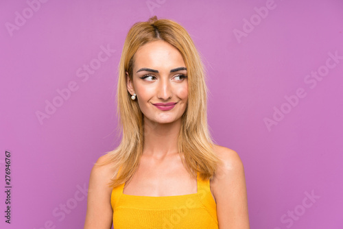 Young blonde woman over purple background standing and looking to the side