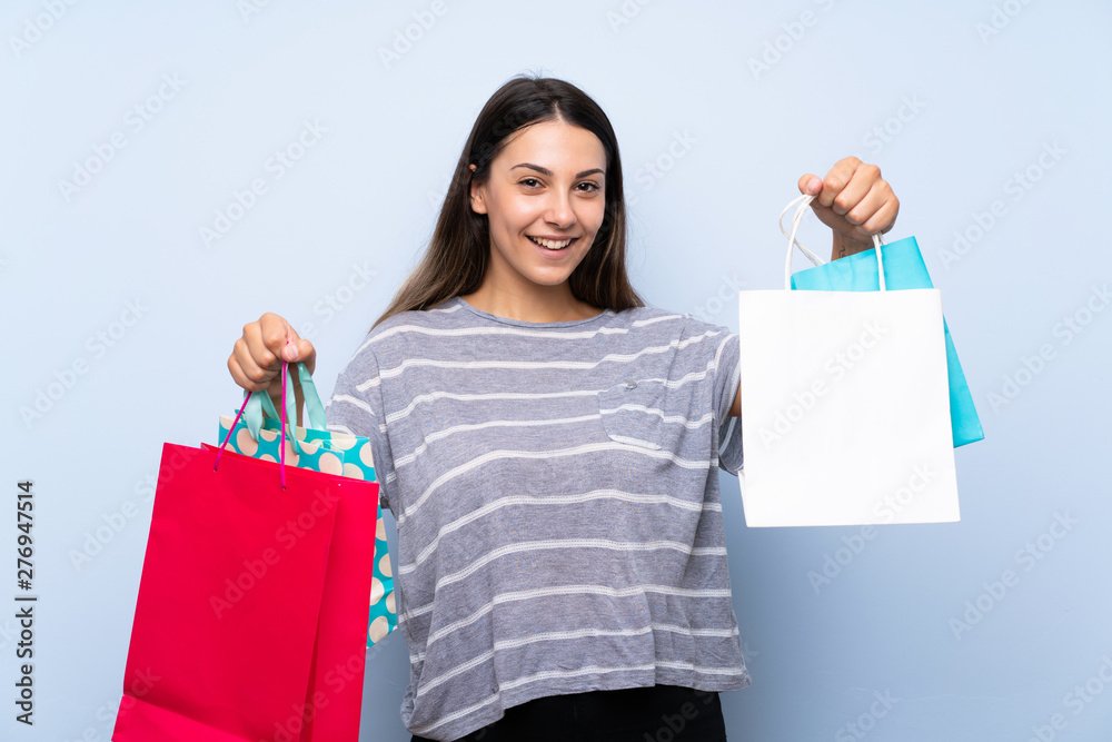 Young brunette woman over isolated blue background holding a lot of shopping bags Young brunette woman over isolated blue background holding a lot of shopping bags