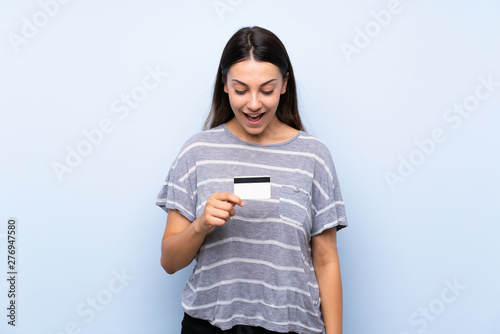Young brunette woman over isolated blue background holding a credit card