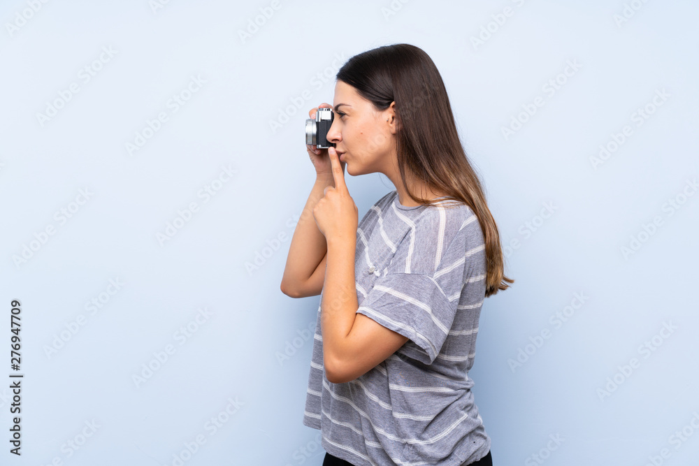 Young brunette woman over isolated blue background holding a camera Young brunette woman over isolated blue background holding a camera