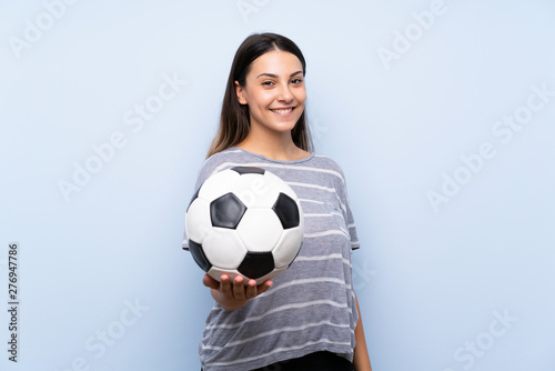 Young brunette woman over isolated blue background holding a soccer ball © luismolinero