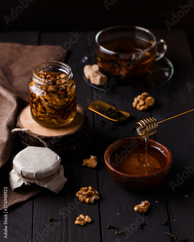 Walnut honey in a small glass jar with a cap of tea beside it on dark wooden background