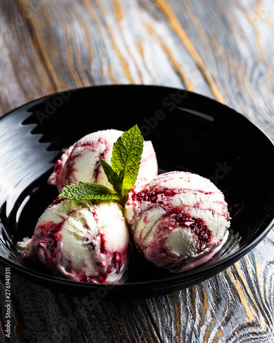 Three strawberry ice cream balls in black bowl with walnuts and mint on black background