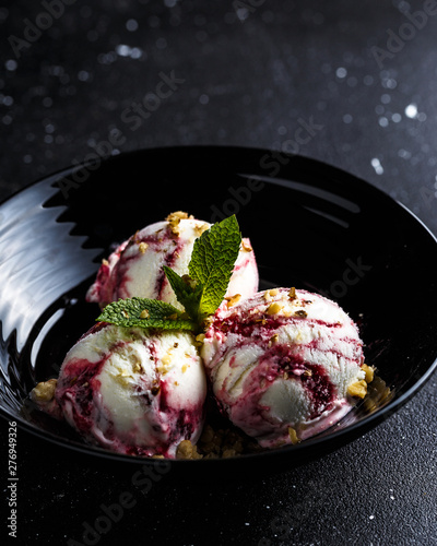 Three strawberry ice cream balls in black bowl with walnuts and mint on black background