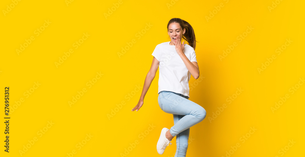 Young woman jumping over isolated yellow wall Young woman jumping over isolated yellow wall